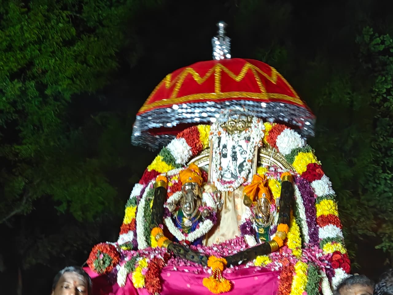 A flower-decorated procession beneath a red ceremonial canopy at night