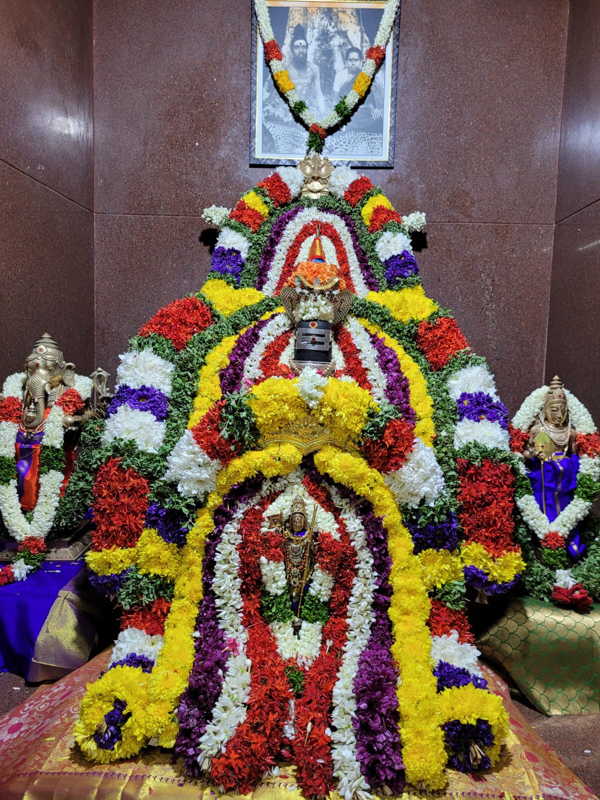 A Shiva lingam and other icons surrounded by colorful flower garlands